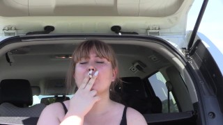 A cute bbw smokes in the street near the car