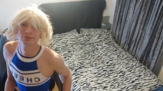 Femboy wearing a fake wig in a cheerleader costume arches over his ass on the bed and rubs it